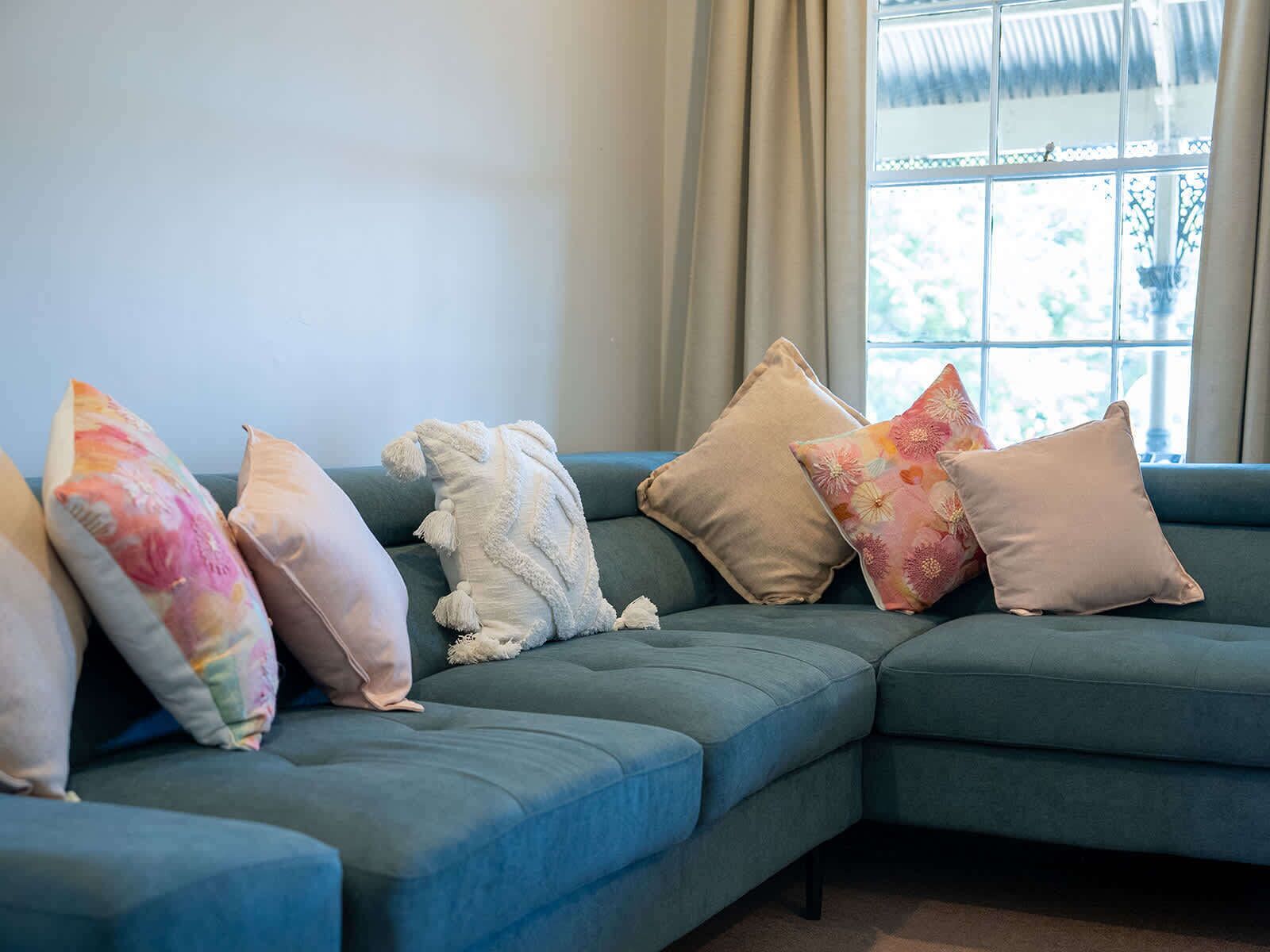 A sectional sofa with multiple cushions in a room with a large window and curtains.