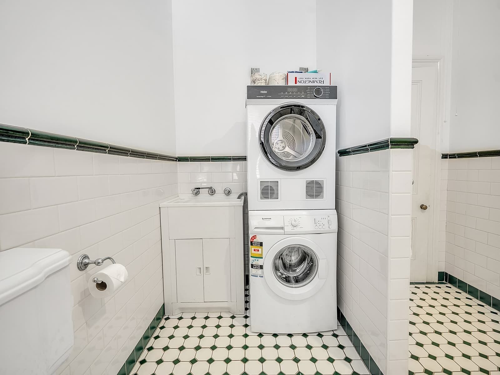 A compact laundry room with a stacked washer and dryer, a small cabinet, and a toilet.