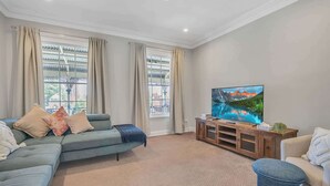 Ein Wohnzimmer mit einer Couch, einem Fernseher und einem Fenster mit Vorhängen.