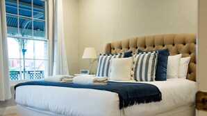 Een netjes opgemaakt bed met een gestuufd hoofdbord, blauw-wit gestreepte kussens en een blauwe dekbedovertrek.