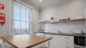 Een moderne keuken met witte kasten, een houten tafel en een raam met zonwering.