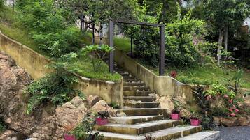 Una escalera de concreto con macetas rosadas, rodeada de follaje y un pequeño elemento acuático.