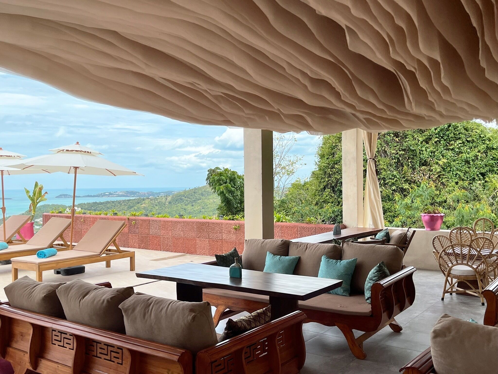 An outdoor seating area with lounge chairs, a table, and umbrellas, overlooking a scenic landscape.