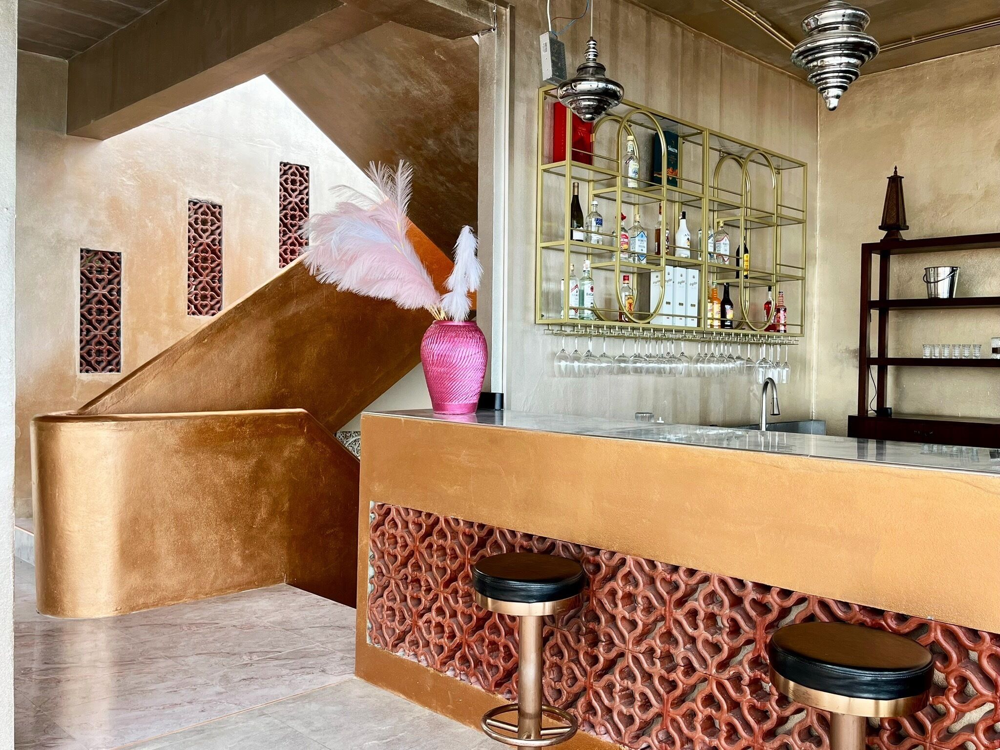 A bar area with a counter, stools, a decorative vase with feathers, and a mirrored shelf with bottles.