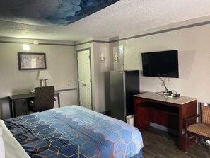 A hotel room with a bed, desk, chair, television, and a door.