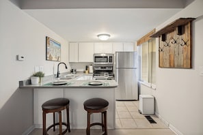 A modern kitchen with white cabinets, stainless steel appliances, and a bar area with stools. - Charming 1-bedroom King condo in Park City perfect for your getaway (Park City)