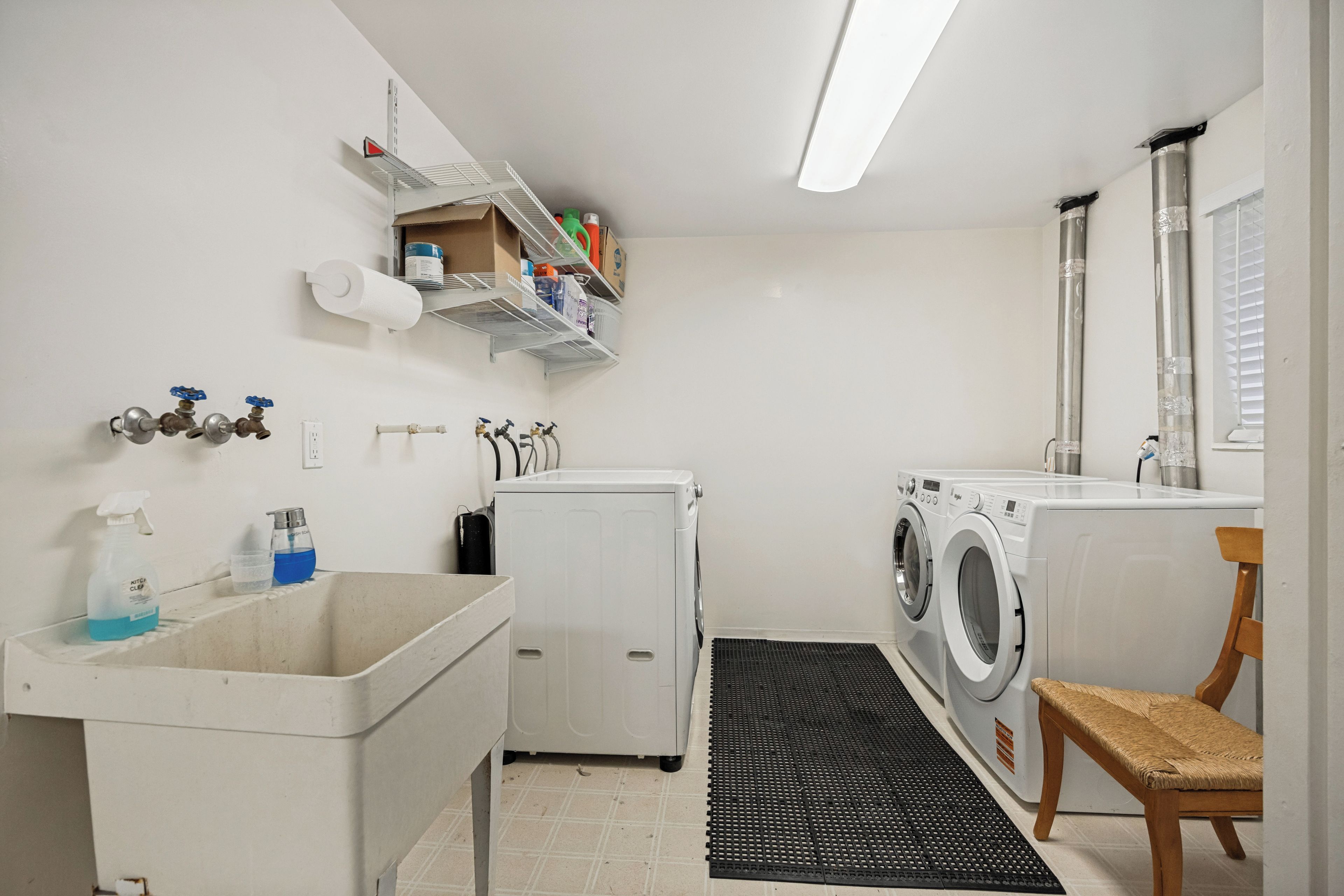 Une buanderie équipée d’un lave-linge, d’un sèche-linge, d’un évier et d’étagères contenant des produits de nettoyage.