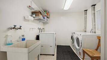 Une buanderie équipée d’un lave-linge, d’un sèche-linge, d’un évier et d’étagères contenant des produits de nettoyage.