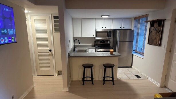 A modern kitchen with white cabinets, stainless steel appliances, and a central island with stools. - Charming 1-bedroom King condo in Park City perfect for your getaway (Park City)