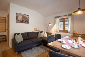 A cozy living room with a dark sofa, a dining table set for tea, and a window with curtains. - Apartment Almwiese, 42 sqm with balcony (Oberaudorf)