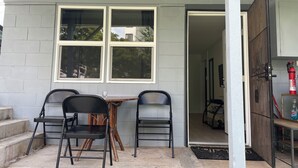 Un patio techado con una mesa y dos sillas, una puerta de madera y un extintor.