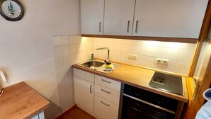 Una cucina compatta con mobili bianchi, un piano di lavoro in legno, un lavello e un fornello.