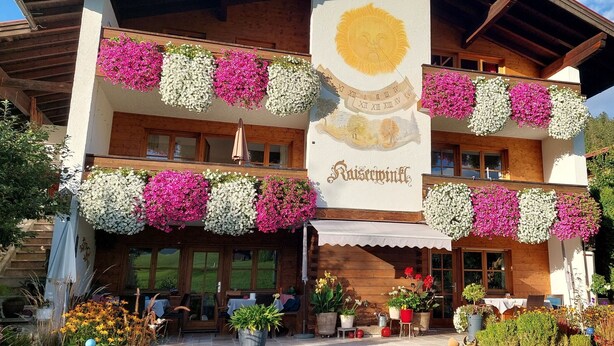 Un hotel con balconi decorati da fiori, una facciata in legno e un cartello con la scritta 'Kaisermühle'.
