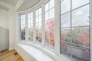 A room with a bay window overlooking a backyard with autumn foliage. - Ravine Getaway | Family & Wedding Retreat – Sleeps 20, 3 Kitchens, Nature Views (Brampton)
