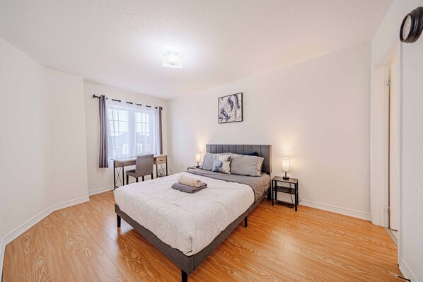 A bedroom with a bed, bedside tables, a desk, and a window with curtains. - Ravine Getaway | Family & Wedding Retreat – Sleeps 20, 3 Kitchens, Nature Views (Brampton)