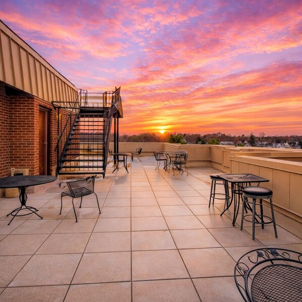 A rooftop terrace with a brick building, a metal staircase, and outdoor seating.