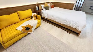 A hotel room with a yellow sofa, a wooden bed, and two framed artworks on the wall. - Raku6 Designer-style Japanese-Western Two-bedroom Ryokan / 15 mins to Shinjuku, (Nakano-ku City)