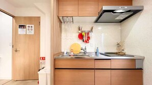 A compact kitchen with wooden cabinets, a stainless steel sink, and a range hood. - Raku6 Designer-style Japanese-Western Two-bedroom Ryokan / 15 mins to Shinjuku, (Nakano-ku City)