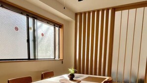 A dining area with a table and chairs, a window with blinds, and a wall with vertical slats. - Raku6 Designer-style Japanese-Western Two-bedroom Ryokan / 15 mins to Shinjuku, (Nakano-ku City)