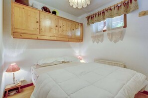 Ein Schlafzimmer mit einem Bett, einer Nachttischlampe, einem Holzschrank und einem Fenster mit Vorhängen.