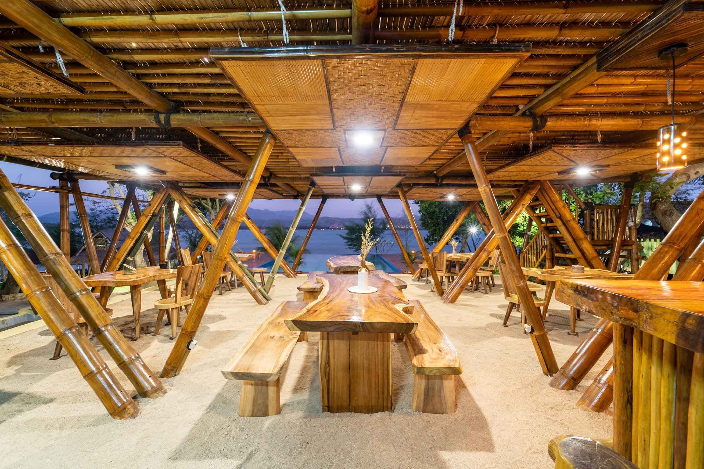 Un espace de restauration extérieur en bois, avec des tables et des bancs, entouré d’une structure en bambou.