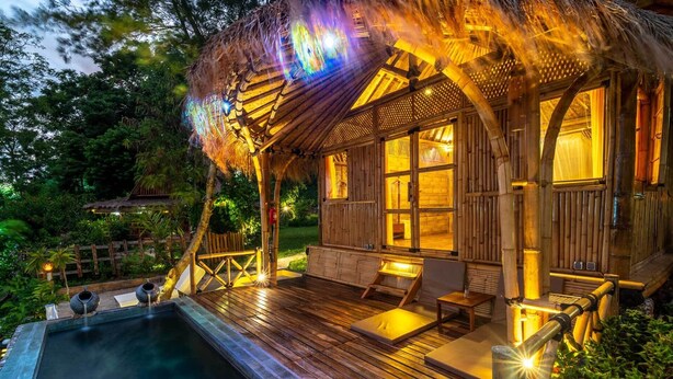 Una cabaña de madera con piscina, terraza y techo de paja.