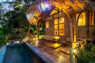 Una cabaña de madera con piscina, terraza y techo de paja.