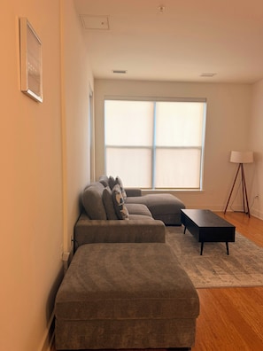 A living room with a sectional sofa, a small side table, and a floor lamp. - Cozy 1-bedroom apartment with AC in delightful Alexandria (Alexandria)