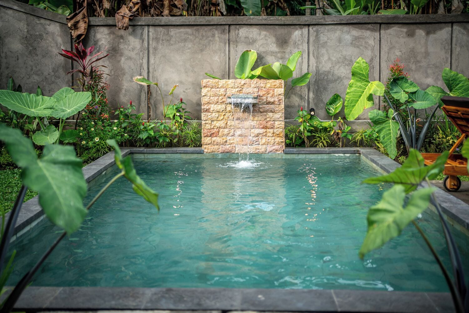Una piscina rettangolare con una cascata in pietra, circondata da una vegetazione lussureggiante.