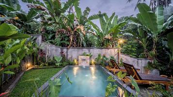A rectangular swimming pool surrounded by lush tropical plants and a stone wall.