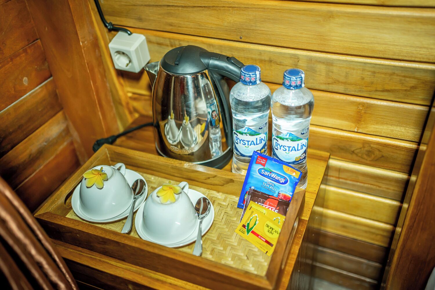 Un intérieur en bois avec un plateau contenant une théière, deux tasses à thé, deux soucoupes, deux bouteilles d’eau et un paquet de collations.