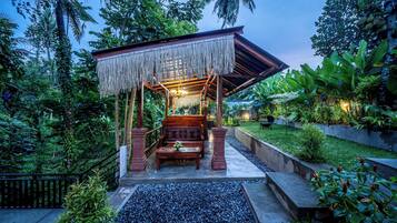 A wooden gazebo with a thatched roof, surrounded by lush greenery and a well-maintained garden.
