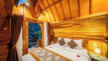 A wooden cabin bedroom with a bed, curtains, a nightstand, and a view of the outdoors.