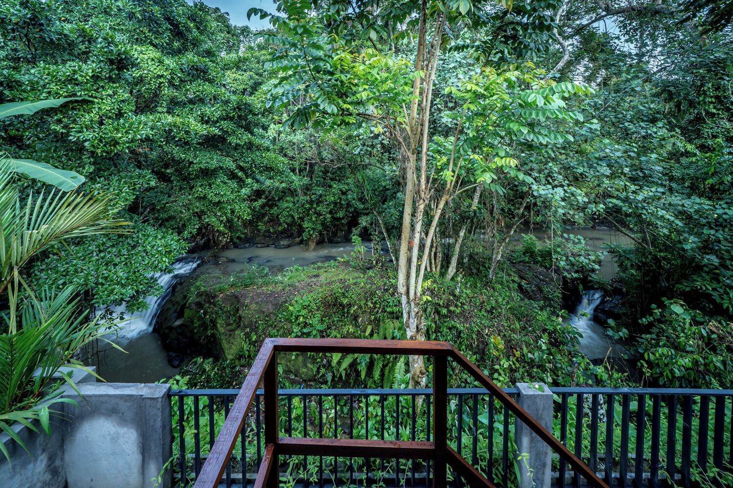 Un exuberante jardín con una cascada, una plataforma de hormigón y una barandilla de metal.
