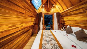 Interior de una cabaña de madera con cama, cortinas y televisor.