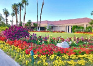 A building with a red-tiled roof, surrounded by a well-maintained garden with various colorful flowers and palm trees. - Private Pool & Spa, Mountain View Villa on the Golf Course 2-bedroom (Cathedral City)