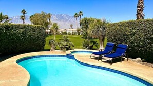 Ein Pool mit blauem Wasser, umgeben von einer geschwungenen Kante. Am Poolufer stehen zwei blaue Liegestühle.