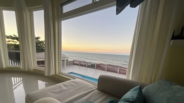 A room with a large window overlooking a pool and the sea.