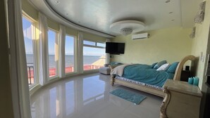 A spacious bedroom with a large bed, a TV, and a view of the sea.
