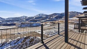 Una terraza de madera con baranda metálica que da a un paisaje nevado con montañas.