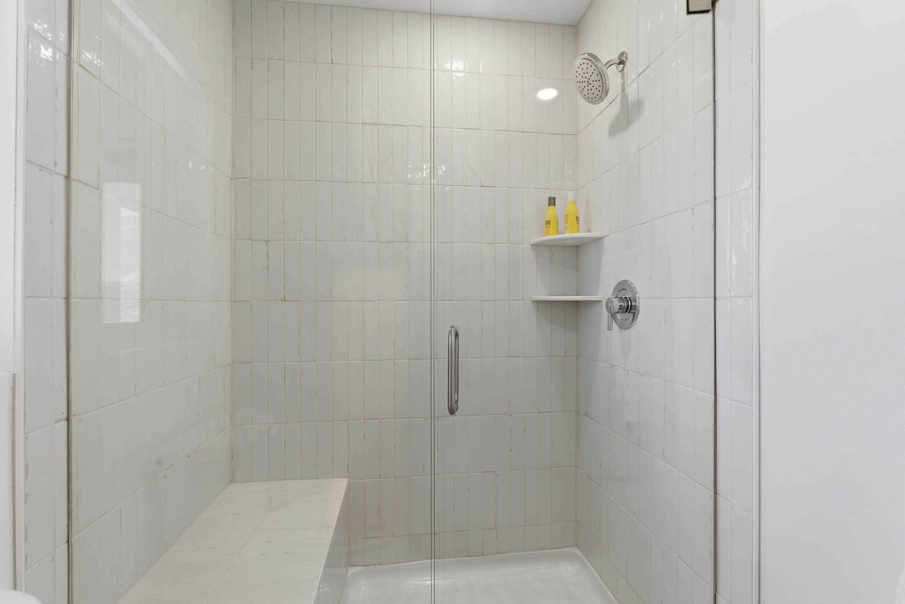 A modern bathroom with white tiles, a glass shower enclosure, and a built-in bench.