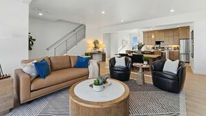 Una sala de estar moderna con un sofá, dos sillones, una mesa de centro y una escalera que sube a un nivel superior.
