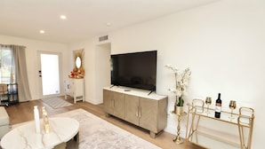 A modern living room with a TV, a white marble table, a gold-framed wine rack, and a large window. - Spacious Luxury Oasis Getaway w/pool 15 mins from beach (Fort Lauderdale)