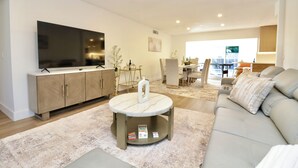 A modern living room with a flat-screen TV, a round coffee table, a sofa, and a dining area with a table and chairs. - Spacious Luxury Oasis Getaway w/pool 15 mins from beach (Fort Lauderdale)