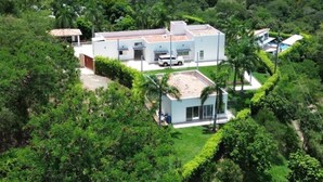 Una casa moderna con garaje cubierto, rodeada de abundante vegetación y una piscina.