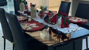 Una mesa de comedor dispuesta con manteles individuales rojos y verdes, cristalería transparente y elementos decorativos.