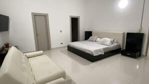 Un dormitorio con cama, una silla, un televisor y una puerta.