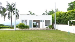Un edificio moderno de una sola planta con amplios ventanales y techo plano, rodeado de un césped cuidado y palmeras.