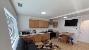 Cozinha compacta com armários de madeira, micro-ondas, fogão e uma TV fixada na parede.