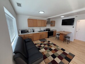 A compact kitchen with wooden cabinets, a microwave, stove, and a TV mounted on the wall. - Completely Updated Darling Home (Milwaukie)